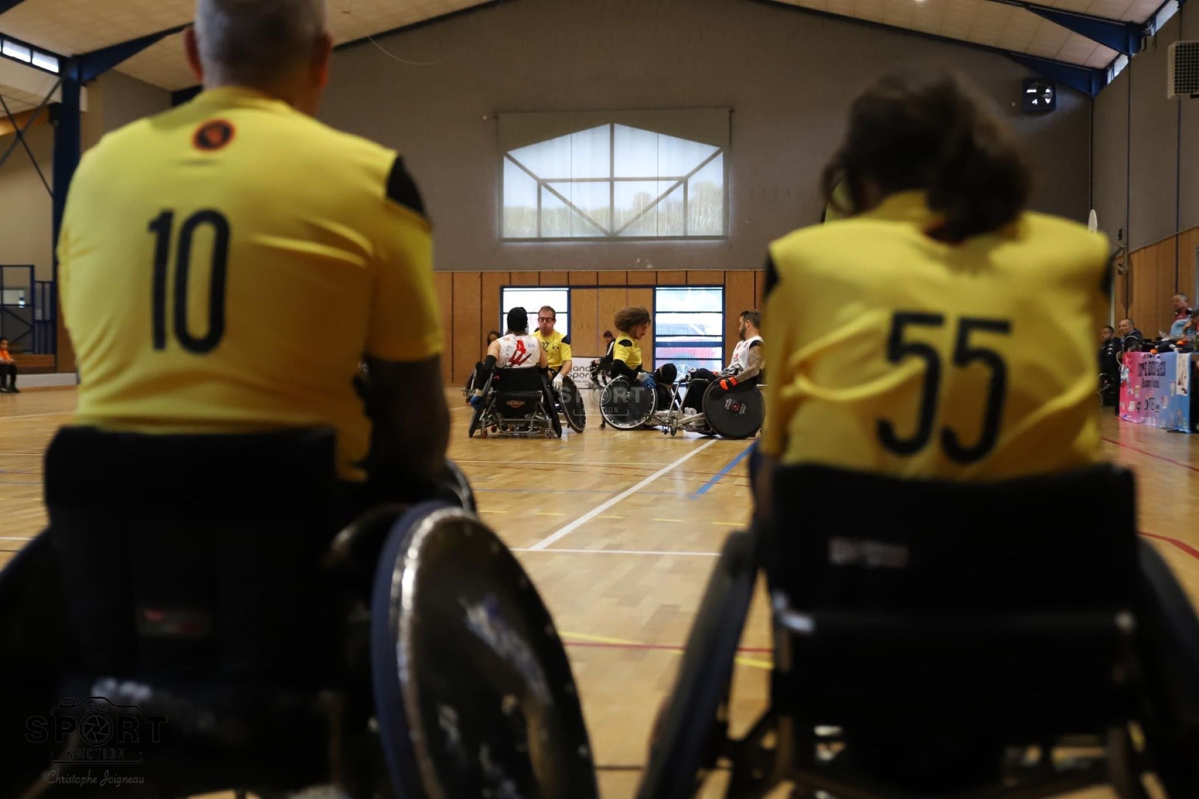 Due giocatori dei Romanes in maglia gialla, numeri 10 e 55, ripresi di spalle mentre dalla panchina guardano i compagni giocare in campo.